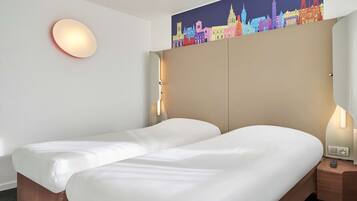 Habitació d'hotel amb dos llits, una obra d'art amb un paisatge urbà a la paret, una làmpada rodona i una tauleta de nit amb una làmpada.