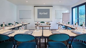 Une salle de conférence équipée d’un écran de projection affichant le mot « Kyriad », de tables avec des bouteilles d’eau, des porte-noms et des chaises.