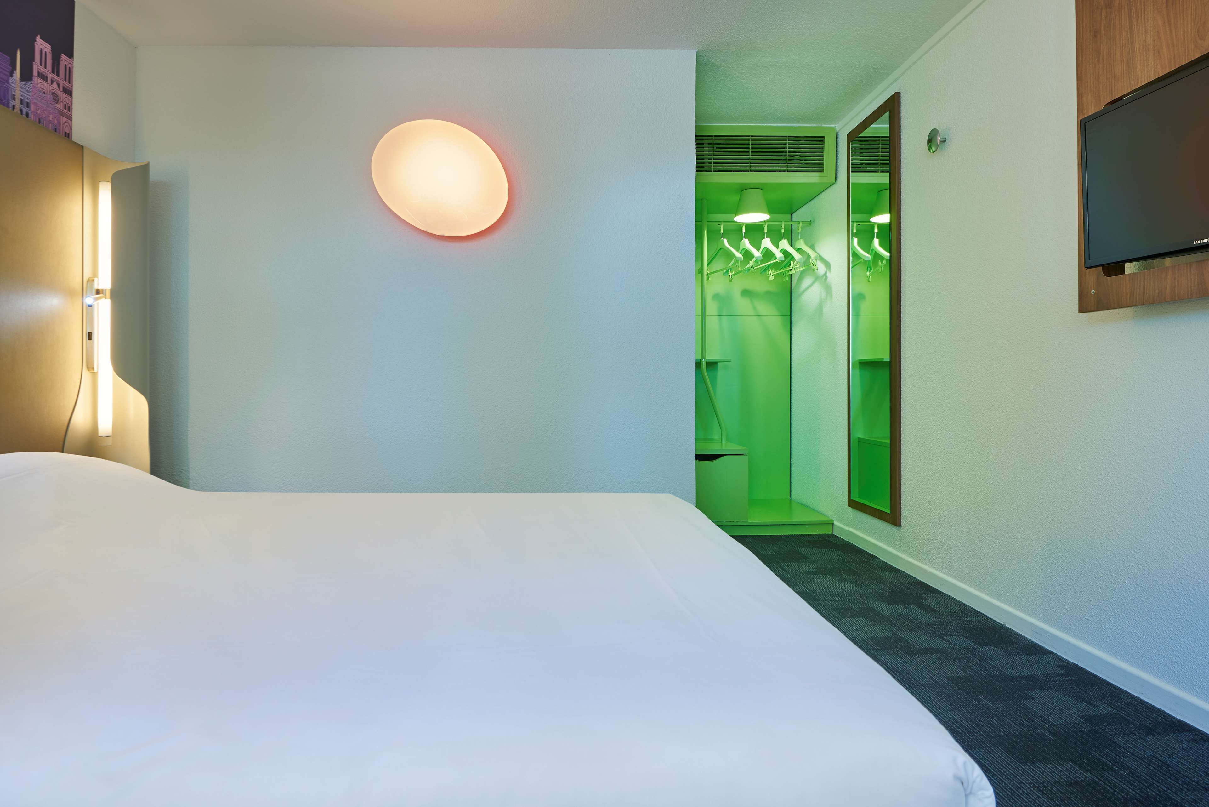 A hotel room with a large bed, a wall-mounted TV, and a green-lit bathroom.