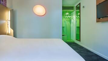 A hotel room with a large bed, a wall-mounted TV, and a green-lit bathroom.