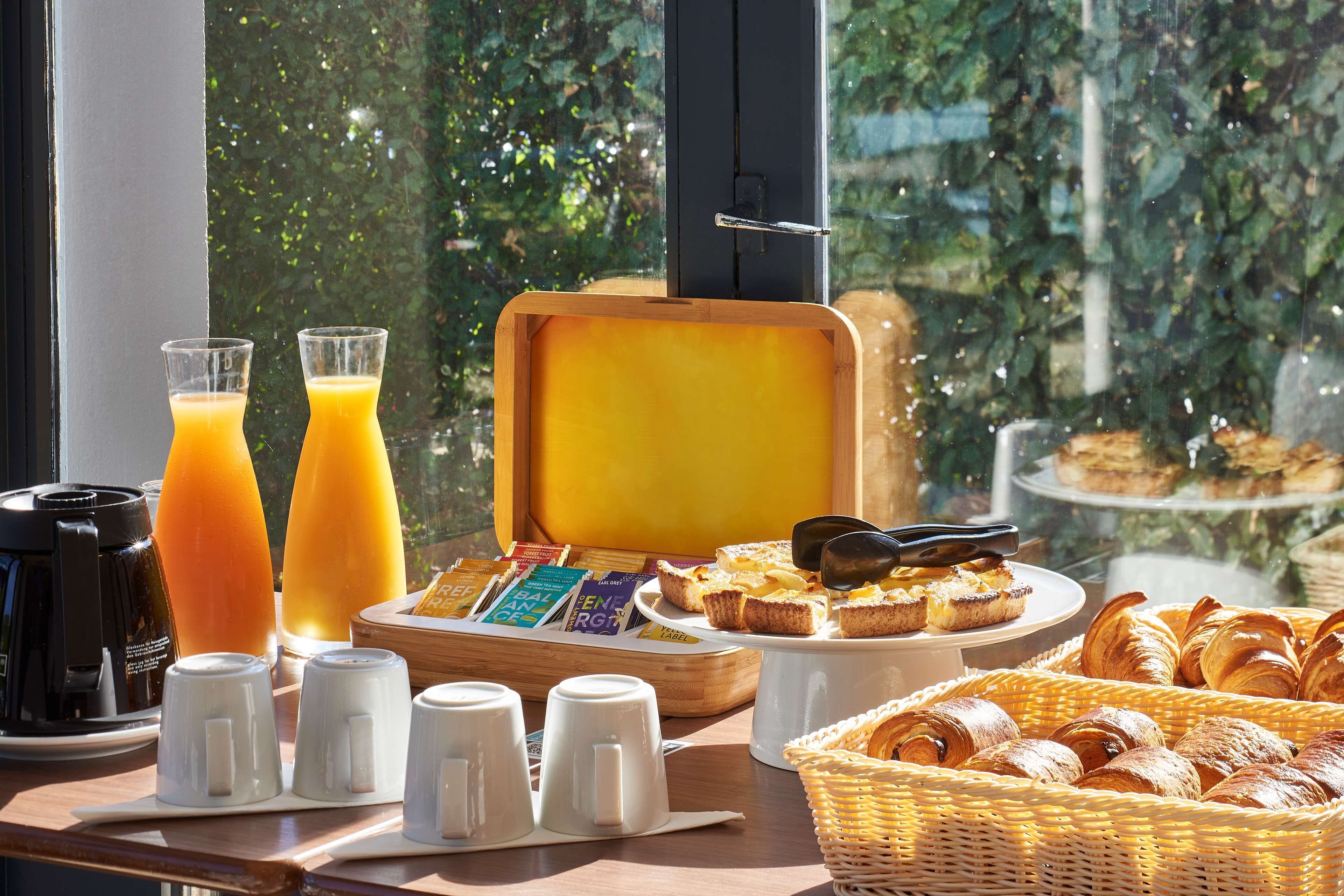 A breakfast buffet with juice, coffee, pastries, and a view of greenery through the window.