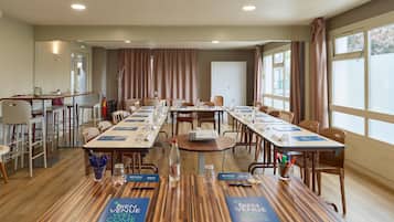 A conference room with long tables, chairs, and a projector. There are welcome signs on the tables and a fire extinguisher in the corner.