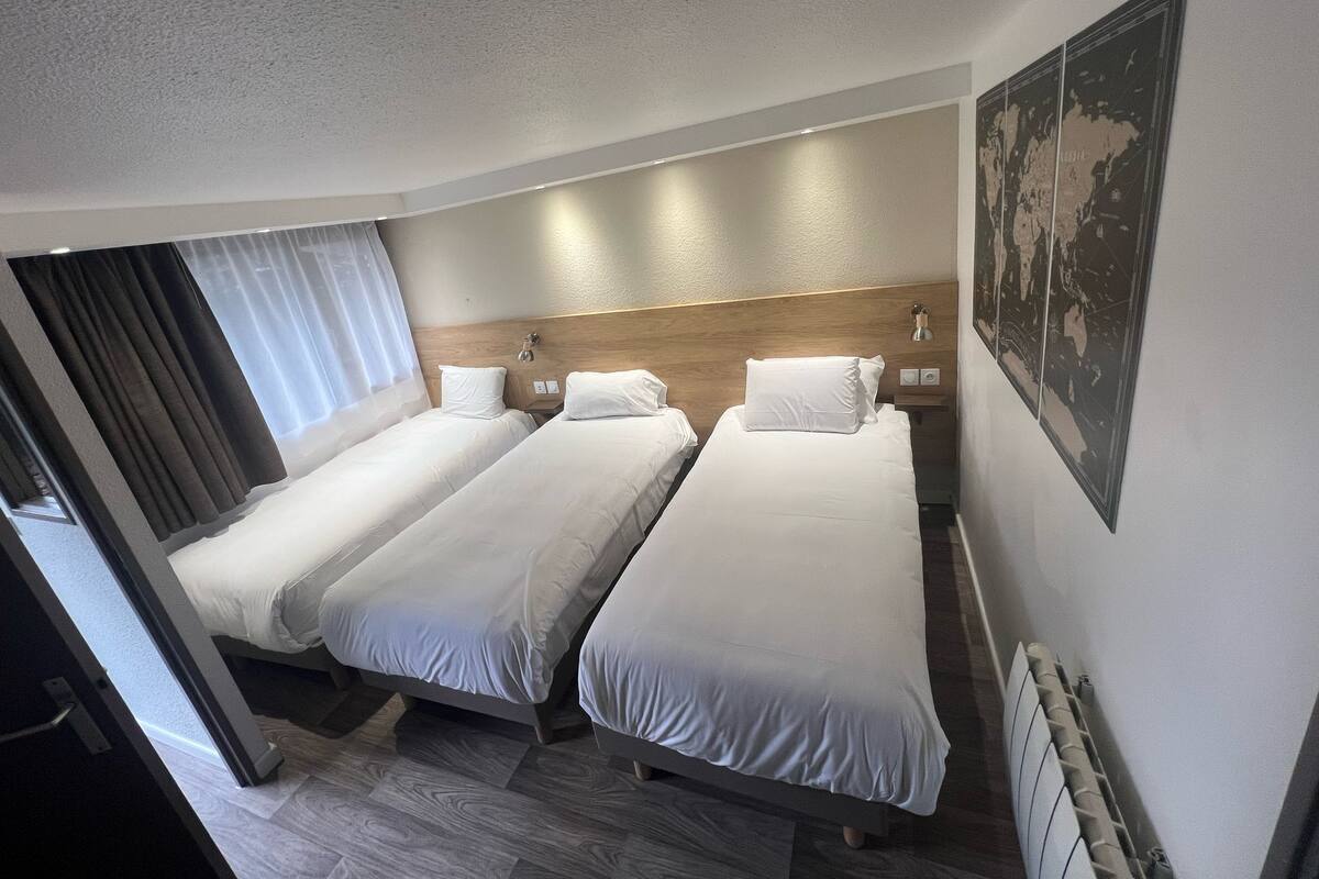 Habitación de hotel con dos camas individuales, cabecero de madera, un mapa en la pared y una ventana con cortinas.