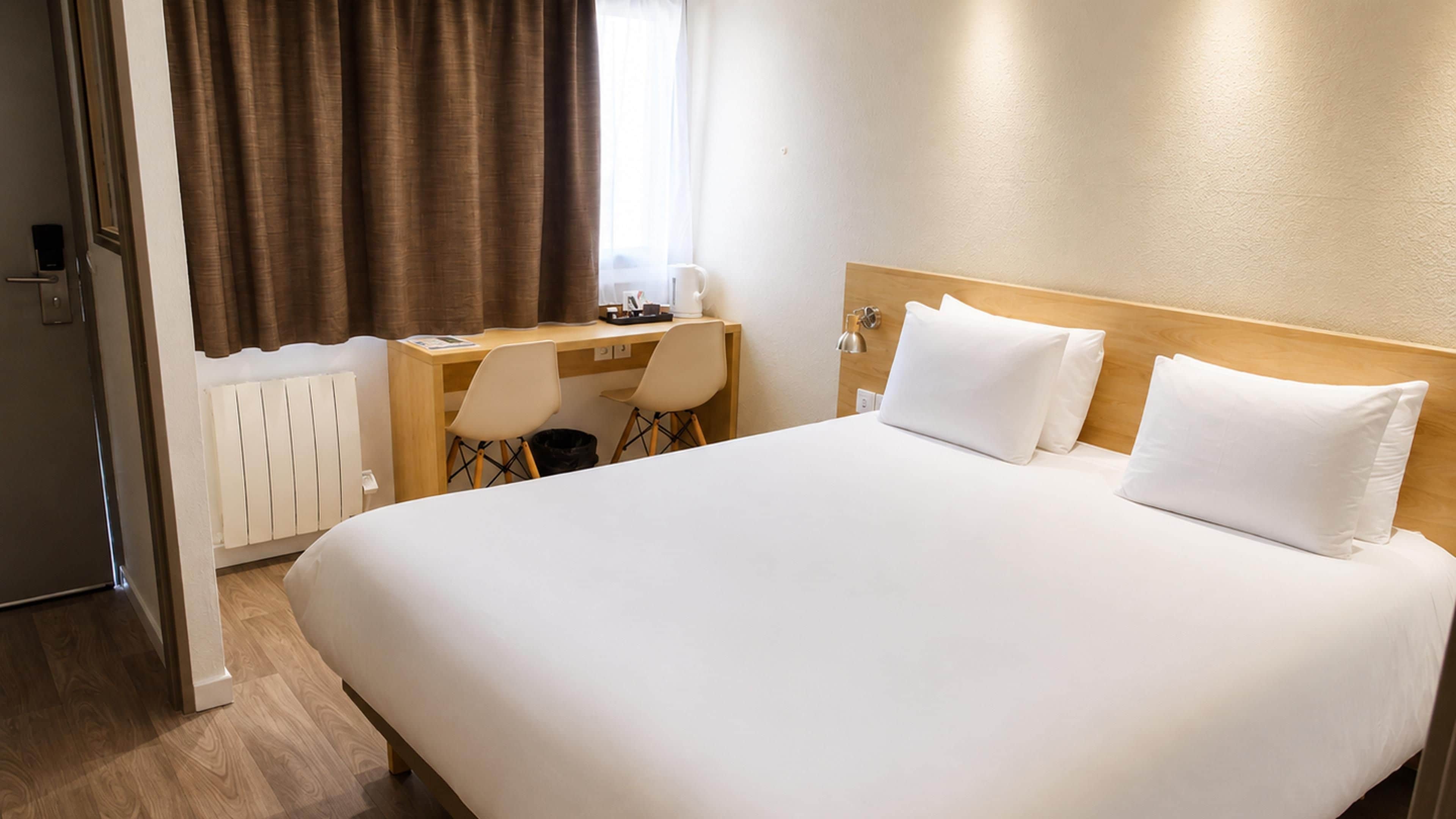 Hotellihuone, jossa on suuri sänky, työpöytä, tuoli ja patteri.