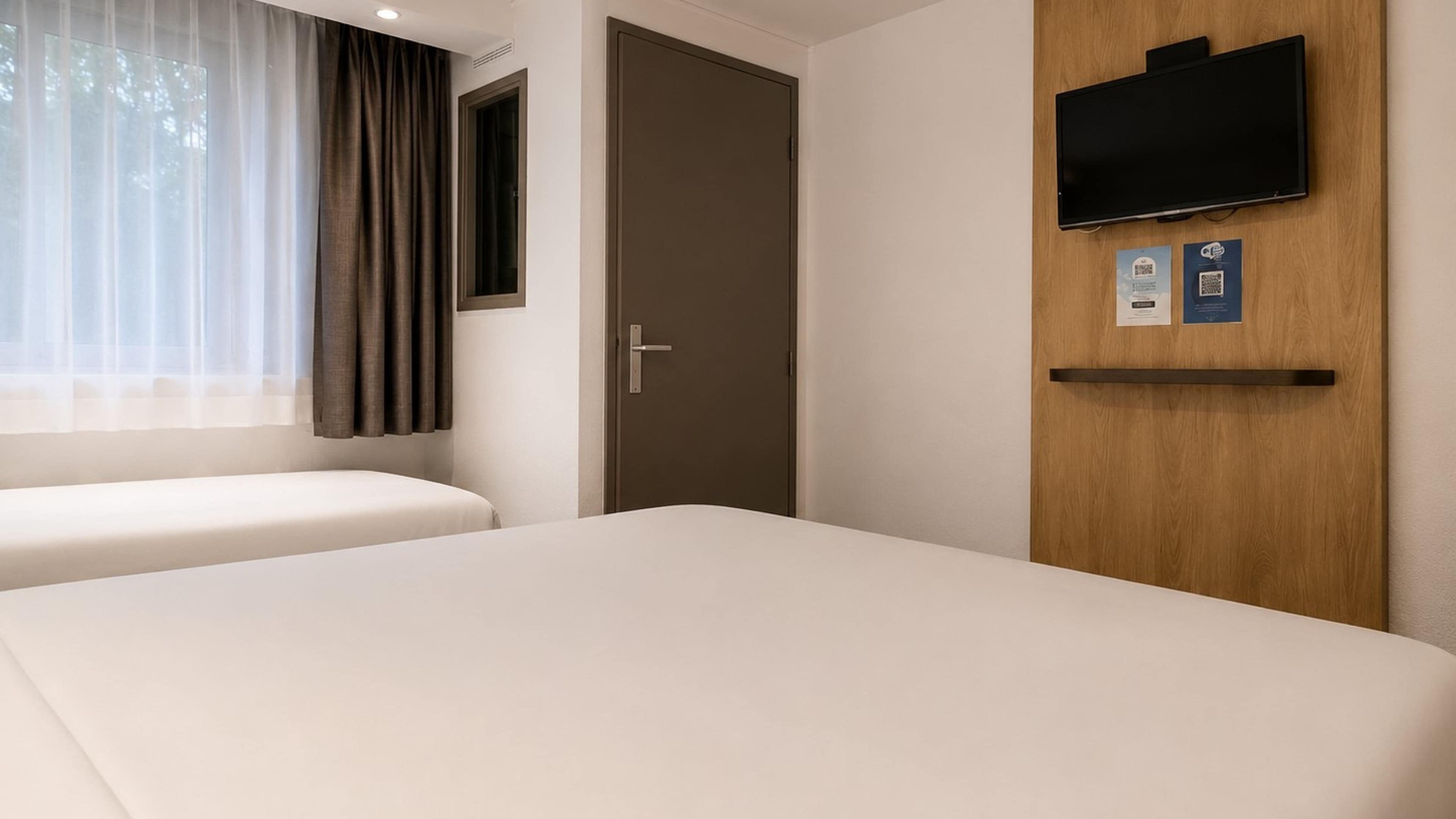 Ett hotellrum med två sängar, en tv som är monterad på väggen och en dörr med ett handtag.