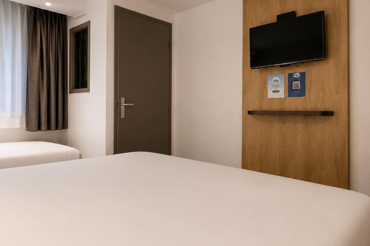 A hotel room with two beds, a television mounted on the wall, and a door with a handle.