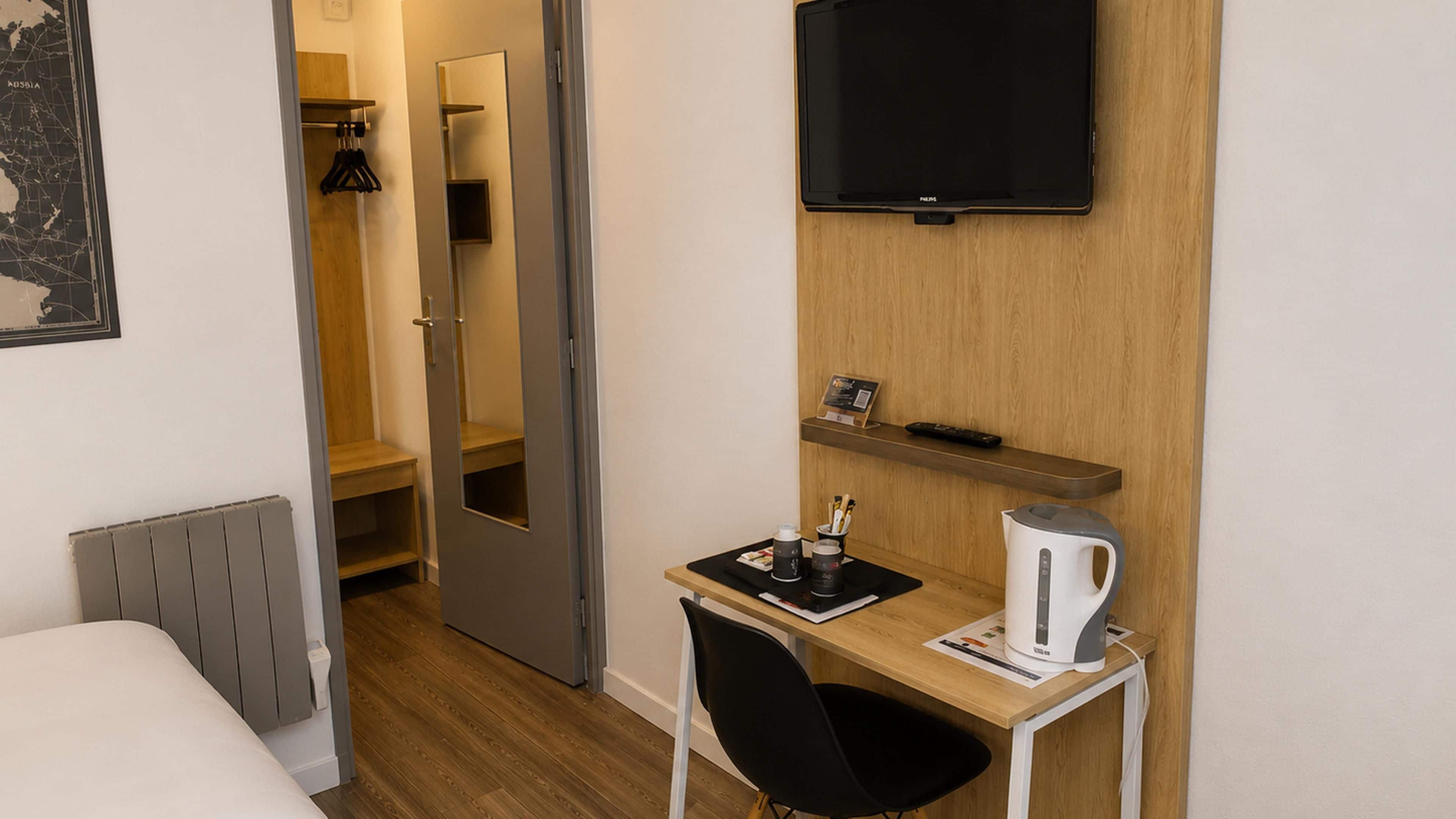 Habitación de hotel con cama, escritorio con tetera, televisión y espejo.