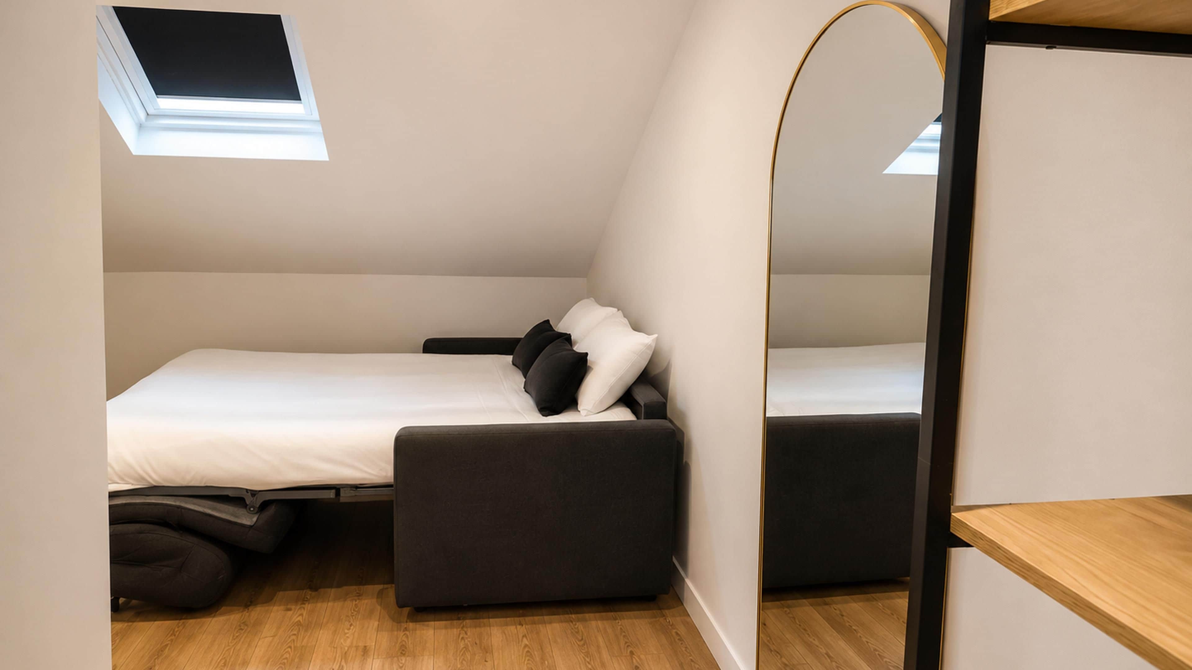 A compact bedroom with a single bed, a small seating area, and a skylight.