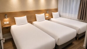 Habitación de hotel con tres camas individuales, cabeceros de madera, lámparas de noche y una ventana con cortinas.