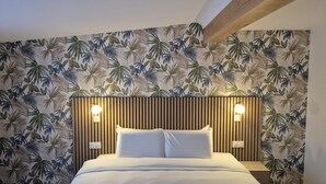 A bedroom with a bed, two bedside lamps, and a wall with a tropical leaf pattern. - Kyriad Fontenay Tresigny (Fontenay-Tresigny)
