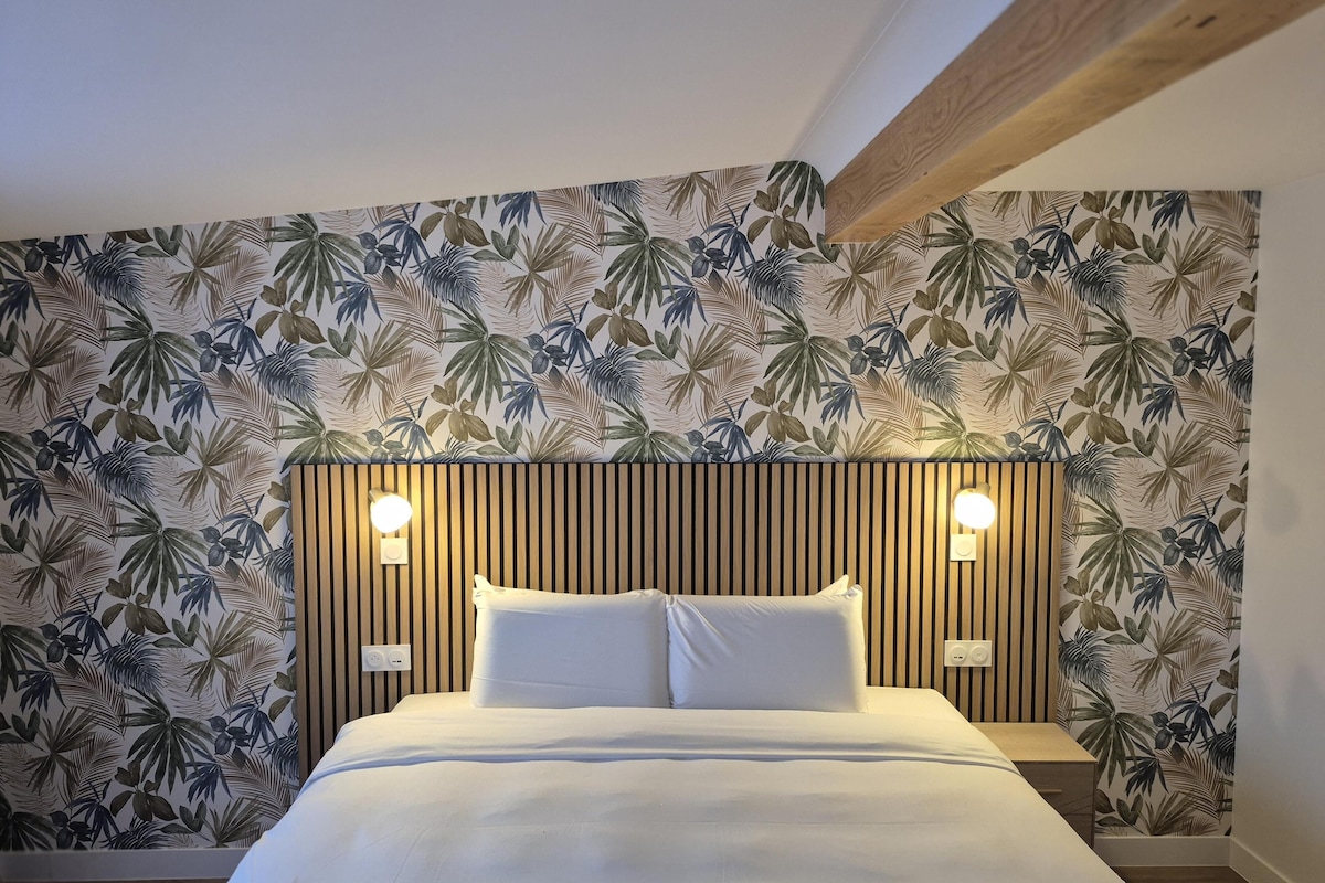 A bedroom with a bed, two bedside lamps, and a wall with a tropical leaf pattern.