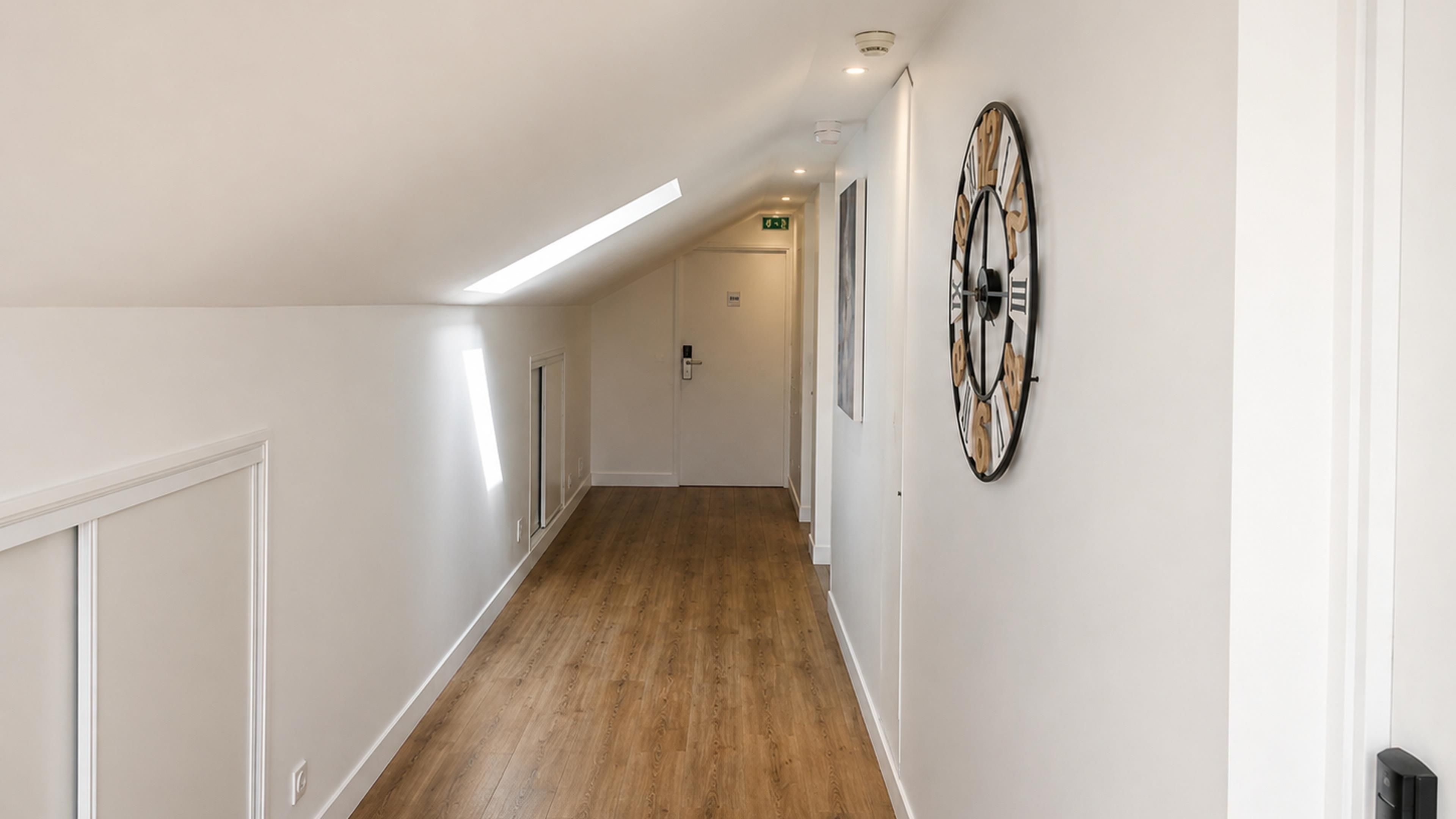Un corridoio con pavimento in legno, pareti bianche e un orologio appeso al muro.