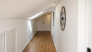 Un pasillo con suelo de madera, paredes blancas y un reloj en la pared.