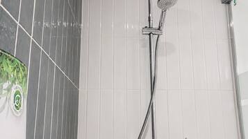 A shower with a handheld showerhead and a hose, against a tiled wall with a green and white pattern.