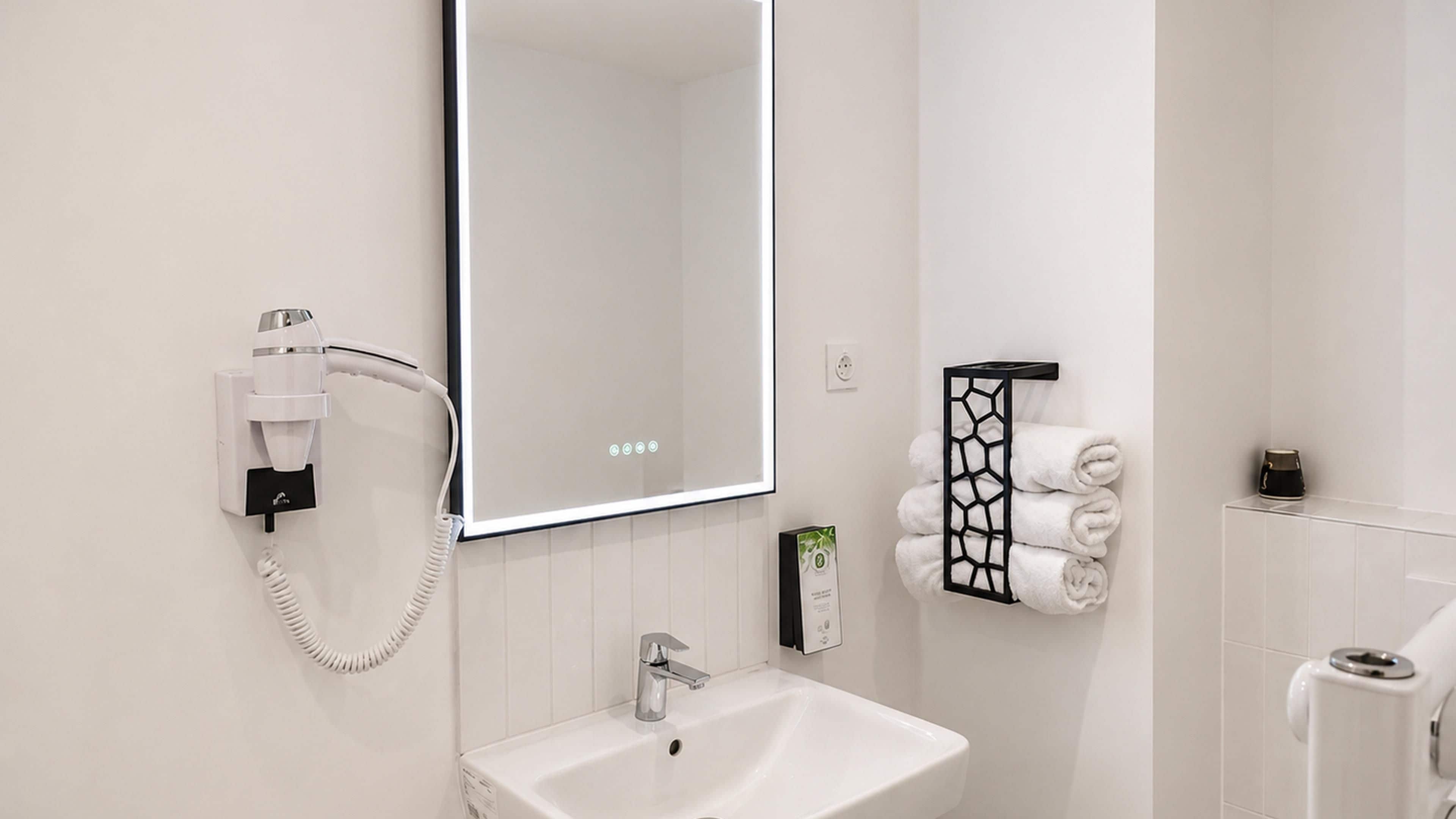 A modern bathroom with a white sink, a mirror, a towel rack, and a hairdryer.