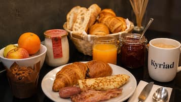 A breakfast setting with croissants, sausages, bacon, a plate of fruit, a cup of coffee, and a jar of jam.