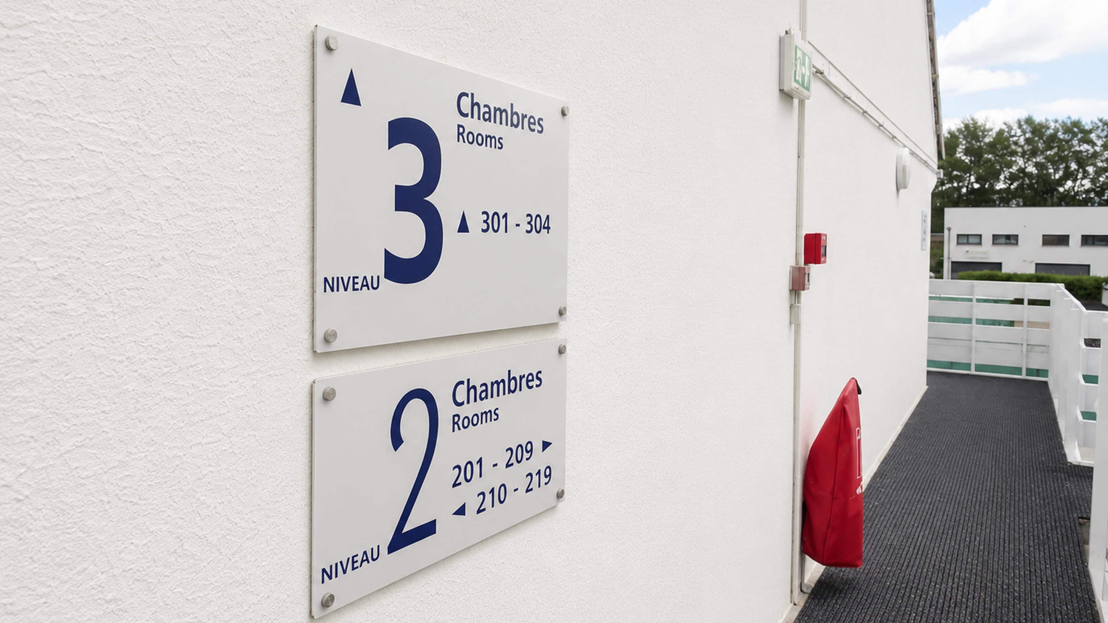 Deux panneaux indiquant les numéros des pièces et les séries de numéros de pièces correspondantes sur la façade d’un bâtiment.