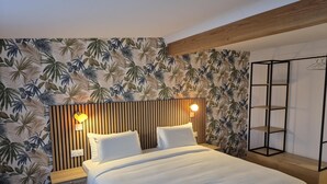 Une chambre d’hôtel comprenant un lit, une table de chevet, une étagère fixée au mur et un mur orné d’un motif de feuilles tropicales.