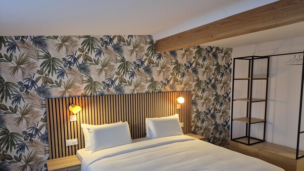 A hotel room with a bed, a nightstand, a wall-mounted shelf, and a wall with a tropical leaf pattern. - Kyriad Fontenay Tresigny (Fontenay-Tresigny)