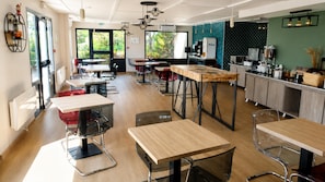 Un café moderno con mesas de madera, sillas de metal y una zona de cocina con electrodomésticos.