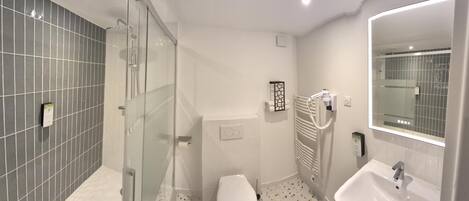 A modern bathroom with a glass-enclosed shower, a white sink, and a large mirror.