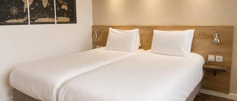 Un lit double avec du linge de lit blanc, une tête de lit en bois, des lampes de chevet et une carte du monde accrochée au mur.