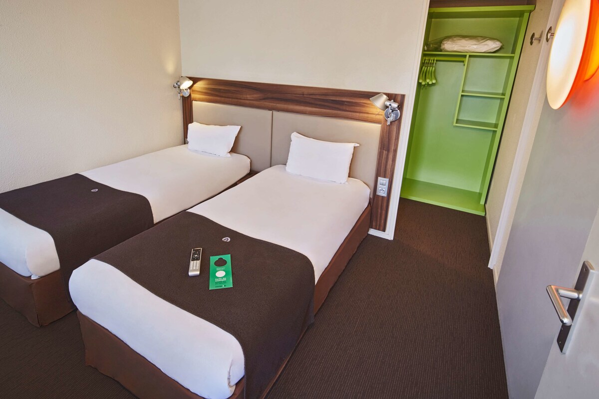 Una habitación de hotel con dos camas, un mueble de almacenamiento verde y la puerta de un baño.