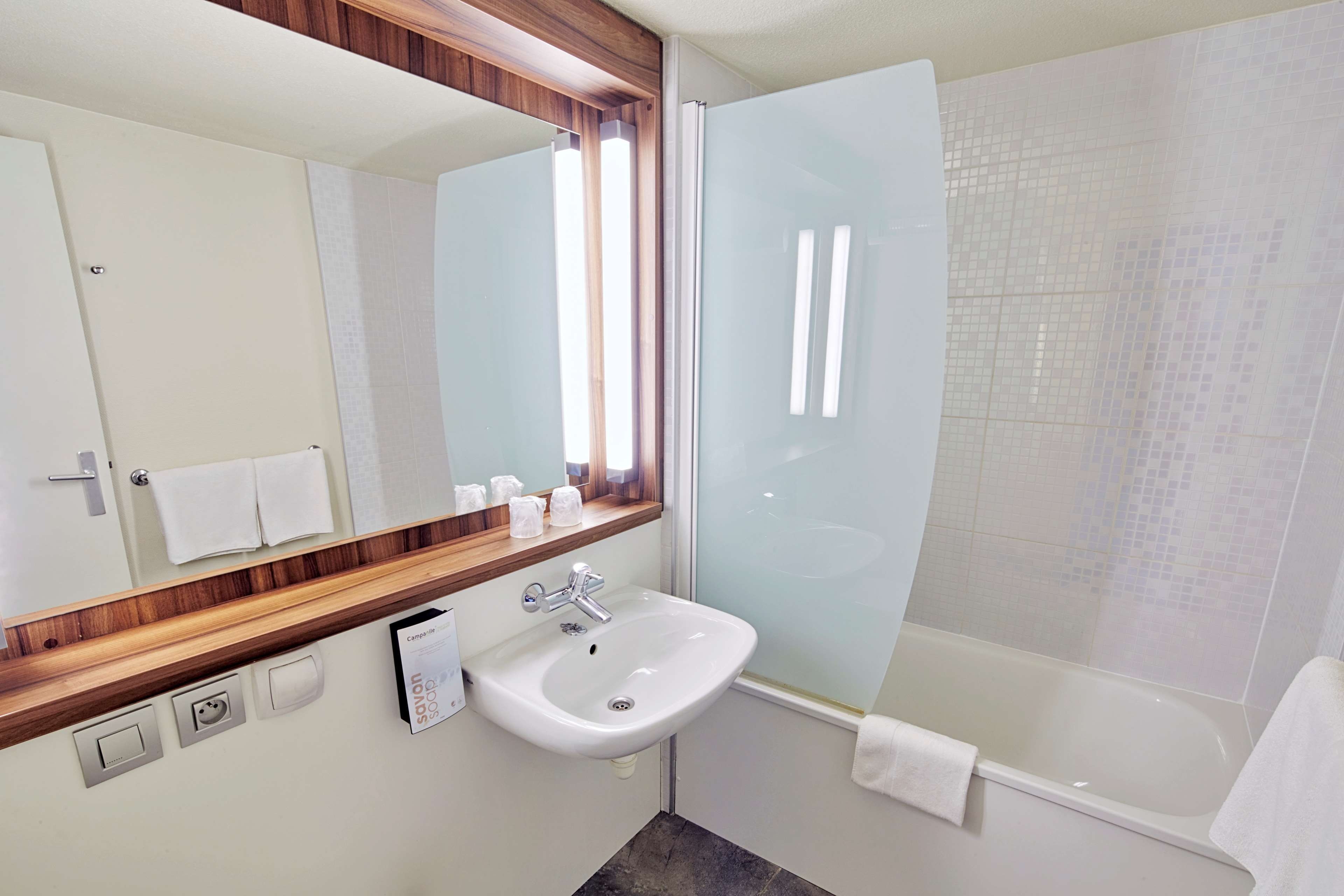 Un baño moderno con un lavamanos blanco, un espejo con marco de madera, una cabina de ducha y una bañera.