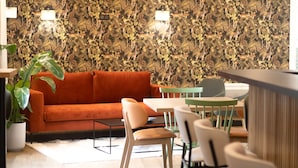 A modern interior with a patterned wall, orange sofa, and a dining area with chairs and a table.