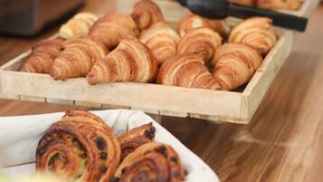 En træbakke med et udvalg af bagværk, herunder croissanter og kanelsnegle, på et træbord.