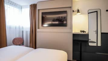 Une chambre d’hôtel moderne avec un grand lit, un téléviseur fixé au mur, une table de chevet avec une lampe et un miroir.