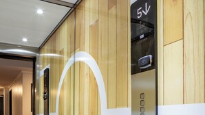 Un ascensor con pantalla digital y botones, ubicado en un pasillo con paneles de madera y un diseño geométrico en la pared.