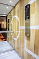 Un ascensor con pantalla digital y botones, ubicado en un pasillo con paneles de madera y un diseño geométrico en la pared.