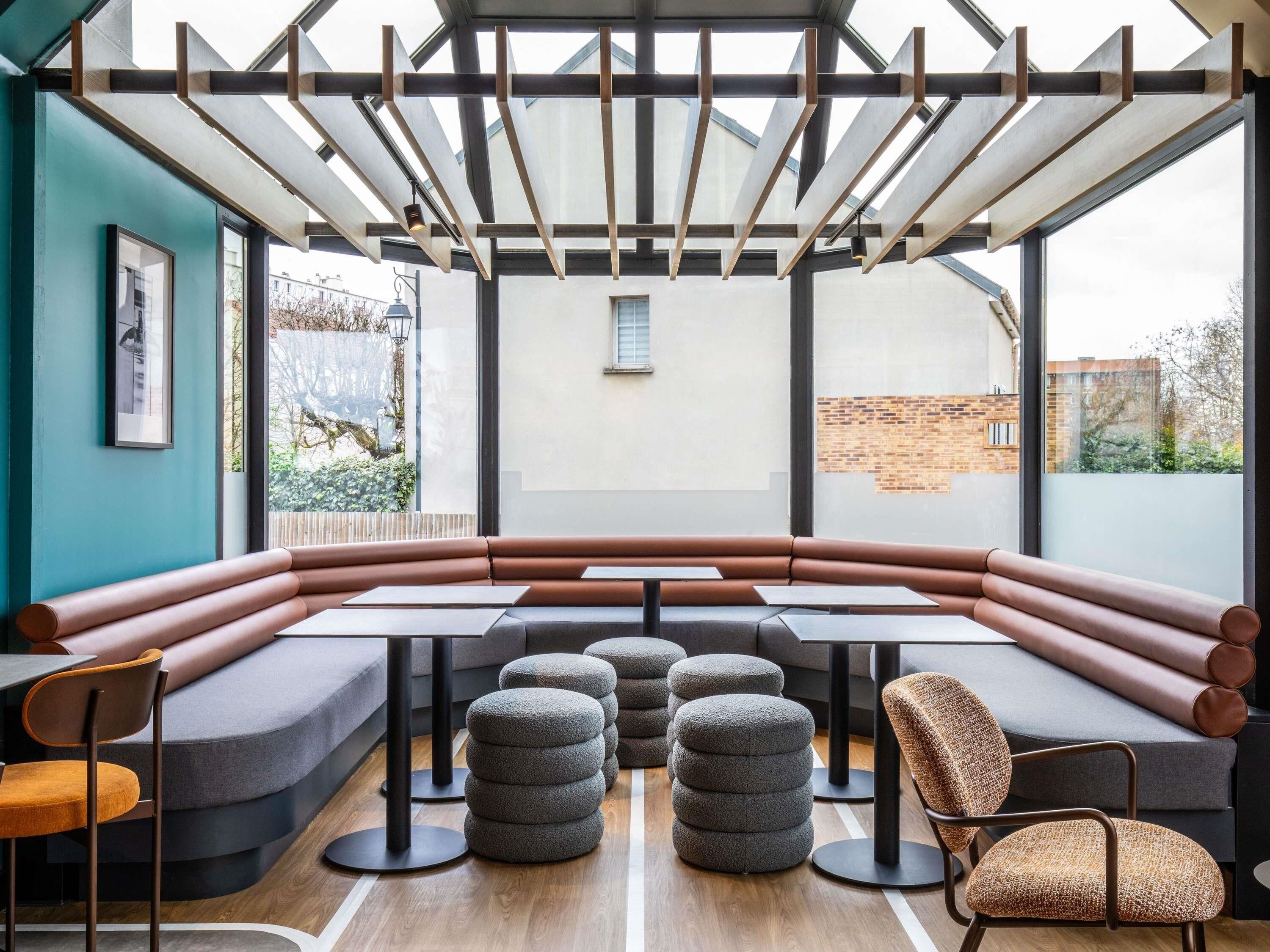 Een modern interieur met een lange tafel, beklede zitplaatsen en ronde poefjes.