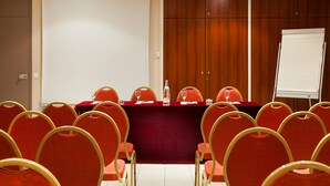 Une salle de conférence avec une longue table, des chaises rouges et un tableau blanc.