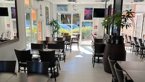 Un restaurant spacieux, doté de nombreuses tables et chaises, de grandes fenêtres offrant une vue sur l’extérieur et de luminaires suspendus.