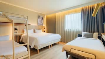 Habitación de hotel con dos camas, una litera, cabecera de madera, un cuadro enmarcado y una ventana con cortinas.