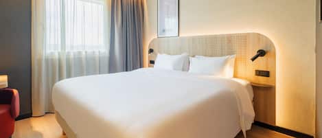 Una cama grande con ropa blanca, un cabecero de madera con diseño perforado, una lámpara de noche y un cuadro en la pared.