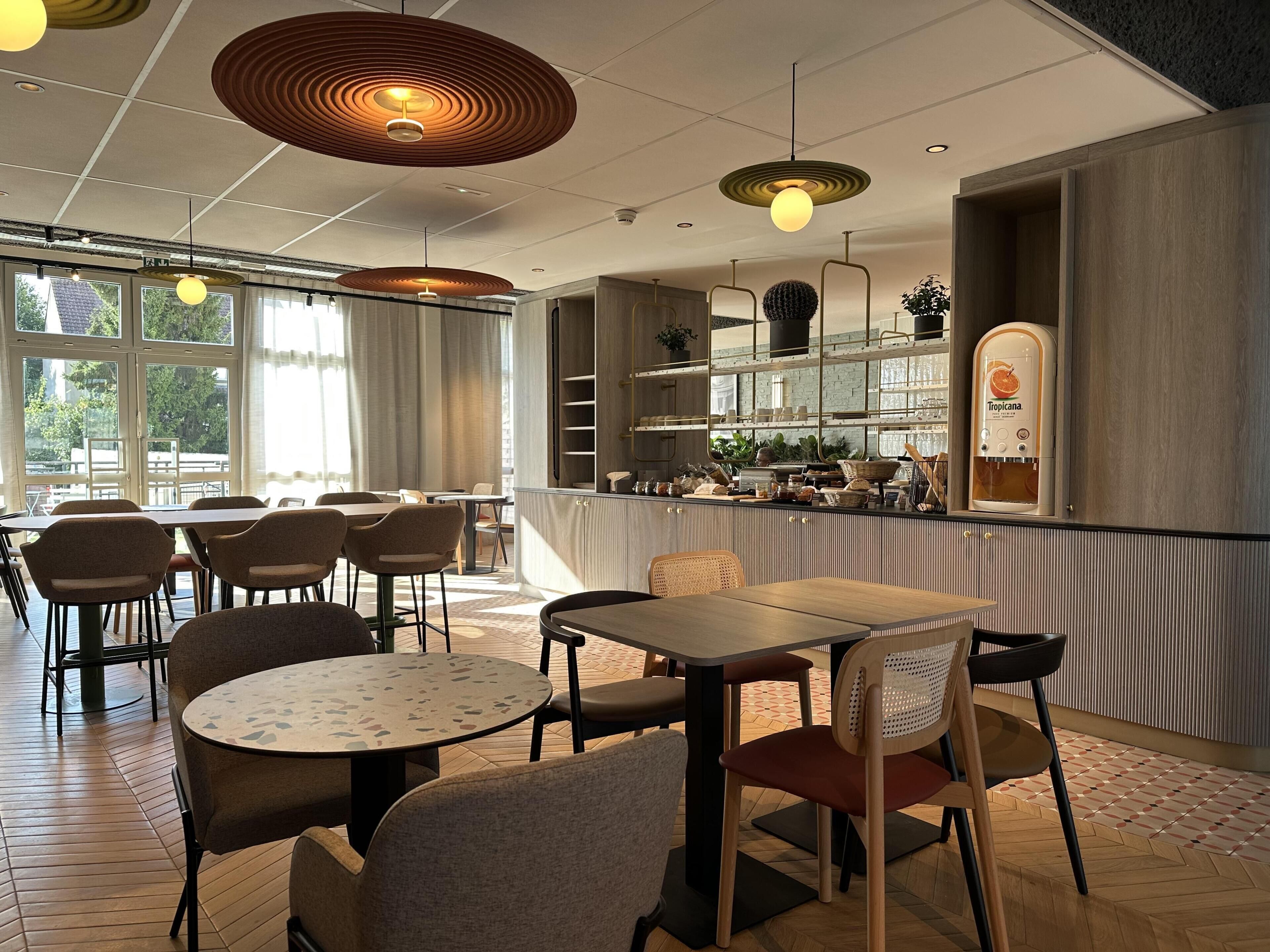 A modern restaurant interior with round tables, chairs, pendant lighting, and a bar area with a water dispenser.