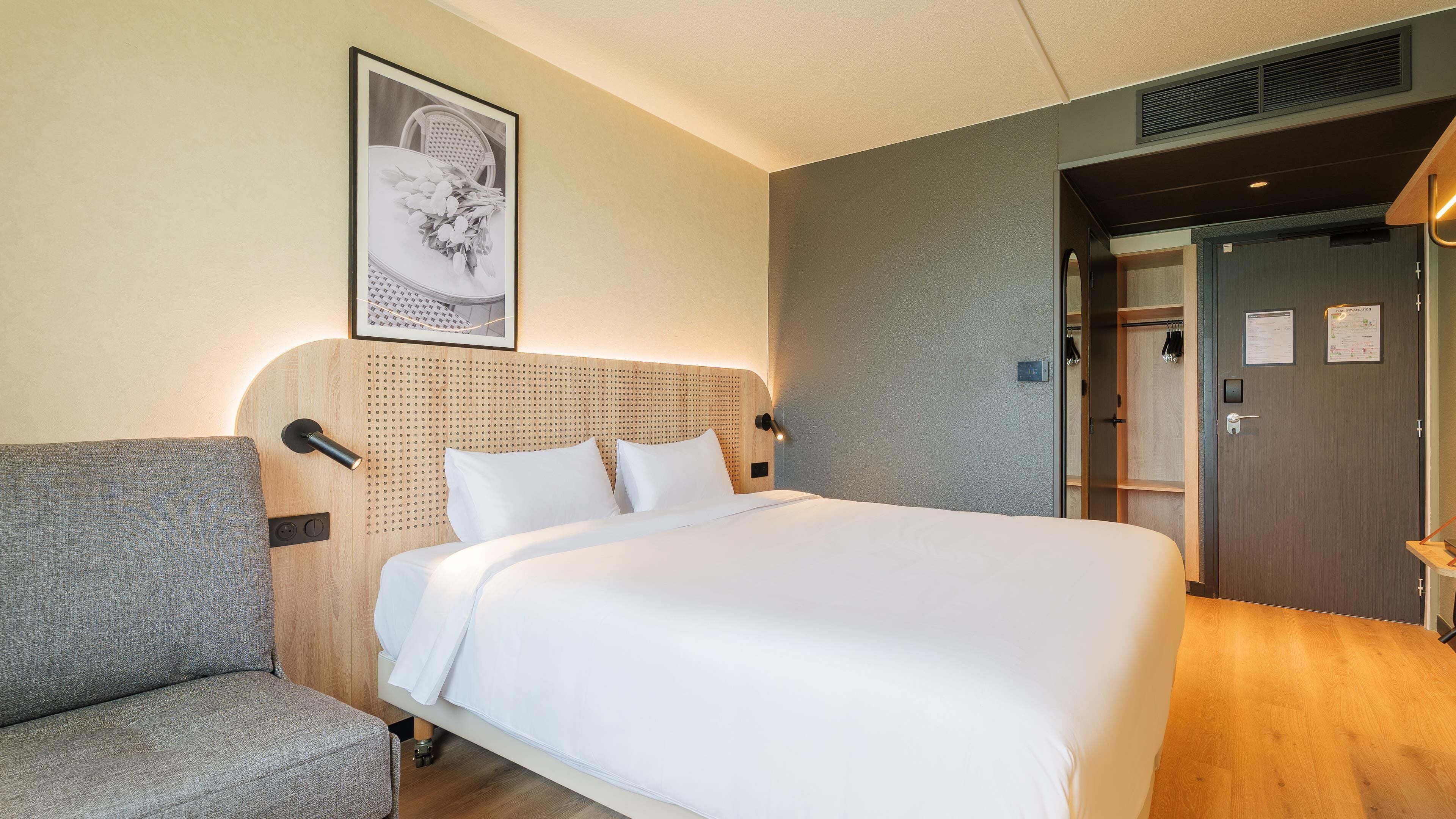 A hotel room with a bed, a sofa, a wall-mounted picture, and a door with a sign.