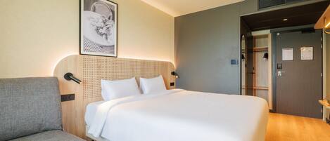 Una habitación de hotel con cama, sofá, un cuadro colgado en la pared y una puerta con un letrero.