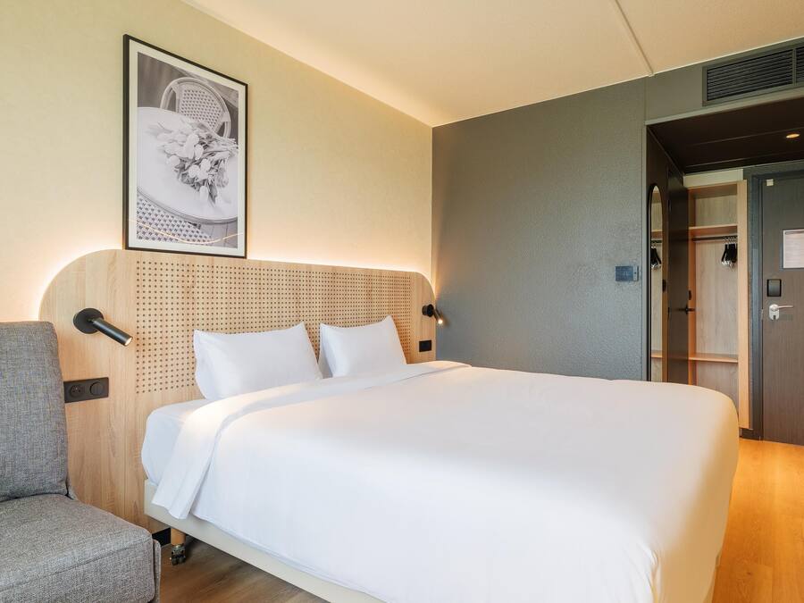 A hotel room with a bed, a sofa, a wall-mounted picture, and a door with a sign.