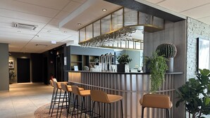 Un bar moderno con taburetes, una barra con cristalería y plantas decorativas.