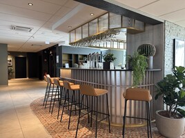 Un bar moderno con taburetes, una barra con cristalería y plantas decorativas.