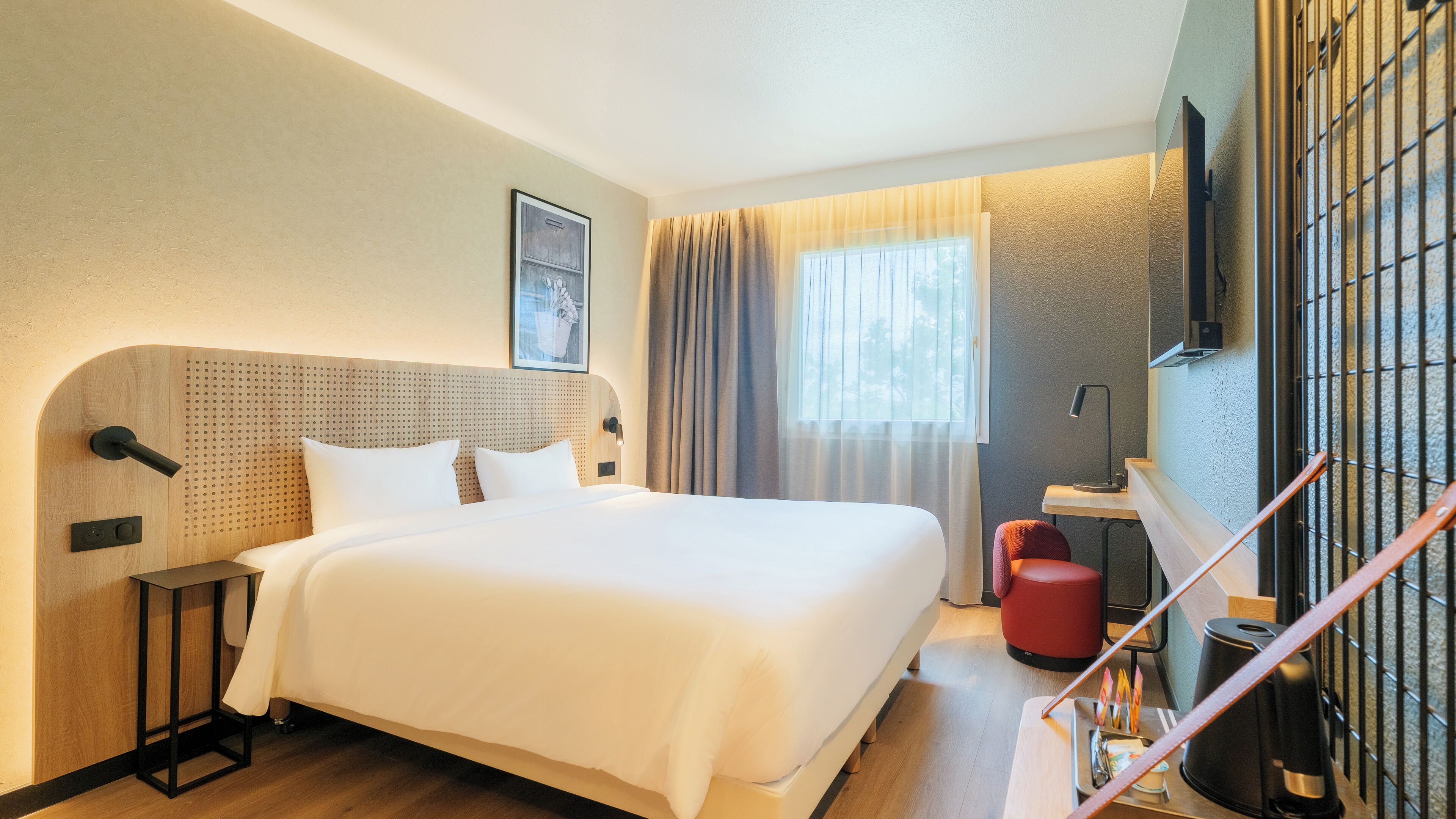 Habitación de hotel con una cama grande, un escritorio, una silla, un televisor y una ventana con cortinas.