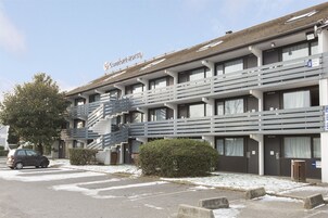 Un hotel de varios pisos con una escalera que conduce a los pisos superiores, un estacionamiento y el suelo cubierto de nieve.