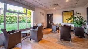 A spacious room with large windows, wicker furniture, and a view of a garden. - Comfort Hotel Rungis Orly (Rungis)