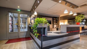 A reception desk with a plant, a red carpet, and a wooden floor. - Comfort Hotel Rungis Orly (Rungis)