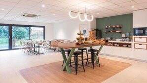 A modern kitchen with a central island, bar stools, and a view of the outdoors. - Hotel Kyriad Argenteuil (Argenteuil)
