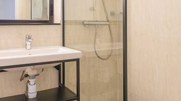 Un baño con ducha de vidrio, lavamanos blanco y espejo.